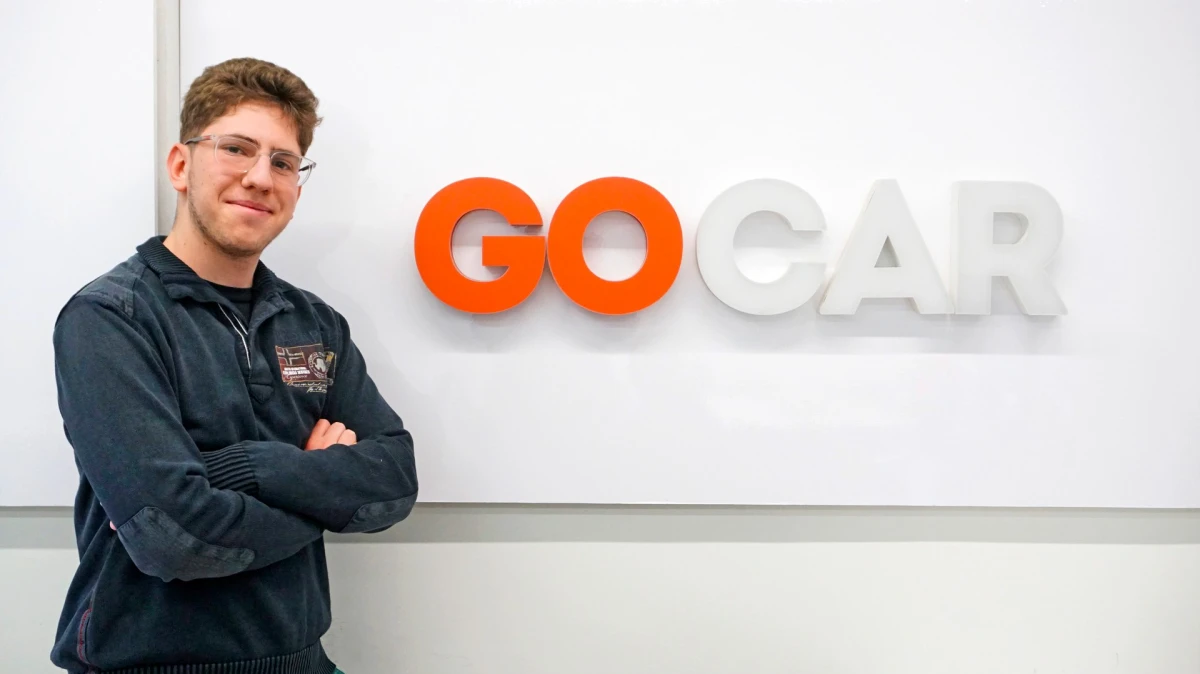 KAR founder standing beside the GOCAR logo at the GOCAR.gr offices